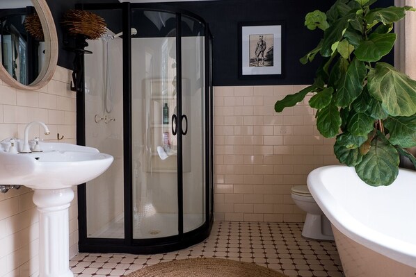 A bathroom with a white pedestal sink, a glass shower enclosure, a toilet, and a large potted plant.