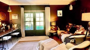 Een gezellige kamer met een plafondventilator, een bed met bloemenbedrukking, een bureau met stoelen en een raam met gordijnen.