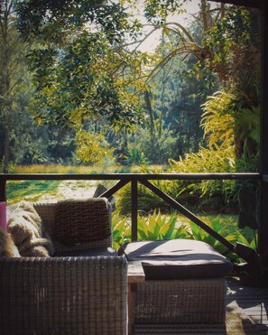 A wicker sofa and ottoman on a wooden deck with a view of a lush garden.