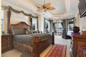 A spacious bedroom with a large bed, a ceiling fan, a treadmill, and a view of the outdoors.