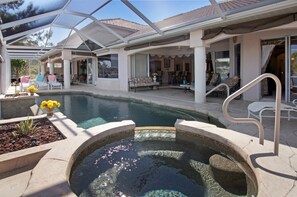 A covered outdoor area with a swimming pool, lounge chairs, and a hot tub.