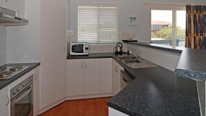 Une cuisine de taille réduite, avec des meubles blancs, une cuisinière, un four à micro-ondes et un évier.