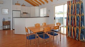Une cuisine spacieuse avec des meubles blancs, une table à manger en bois et des chaises bleues, ainsi qu’une grande fenêtre avec des stores.