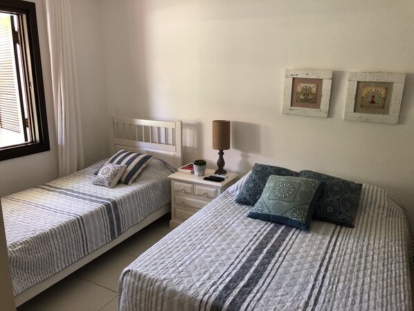 A bedroom with two single beds, a nightstand with a lamp, and a window with curtains.