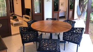 Una mesa de madera redonda con seis sillas negras, una hamaca y vistas a un dormitorio con cama y ventana.