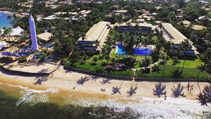 Vista aérea de un complejo turístico con varias construcciones, una playa y una amplia zona de piscina.