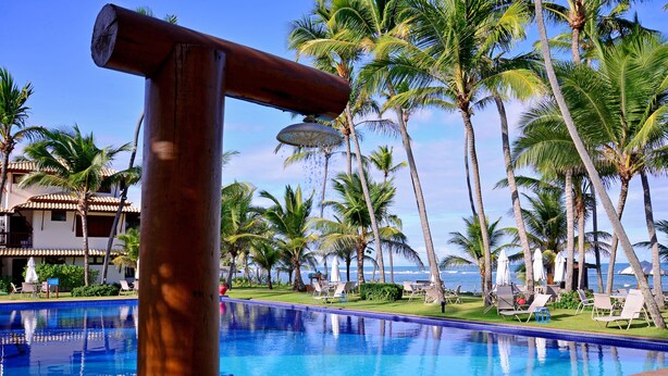 Una piscina con estructura de madera, rodeada de palmeras y vista al océano.