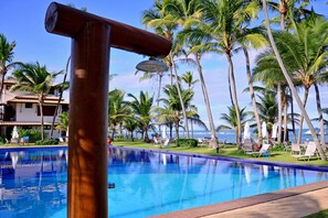 A swimming pool with a wooden structure, surrounded by palm trees and a view of the ocean.