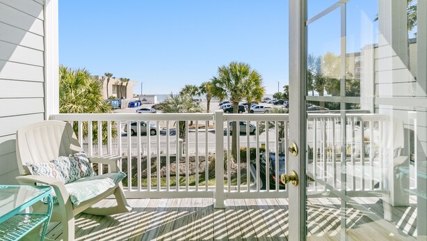 A balcony with a view of a parking lot and palm trees. - Pavilion Watch 2B - Oceanview Condo - Pool - Central Location - Elevator (Folly Beach)