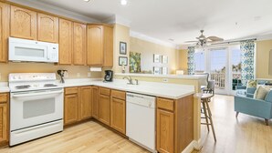 A kitchen with wooden cabinets, a white microwave, and a dishwasher. - Pavilion Watch 2B - Oceanview Condo - Pool - Central Location - Elevator (Folly Beach)