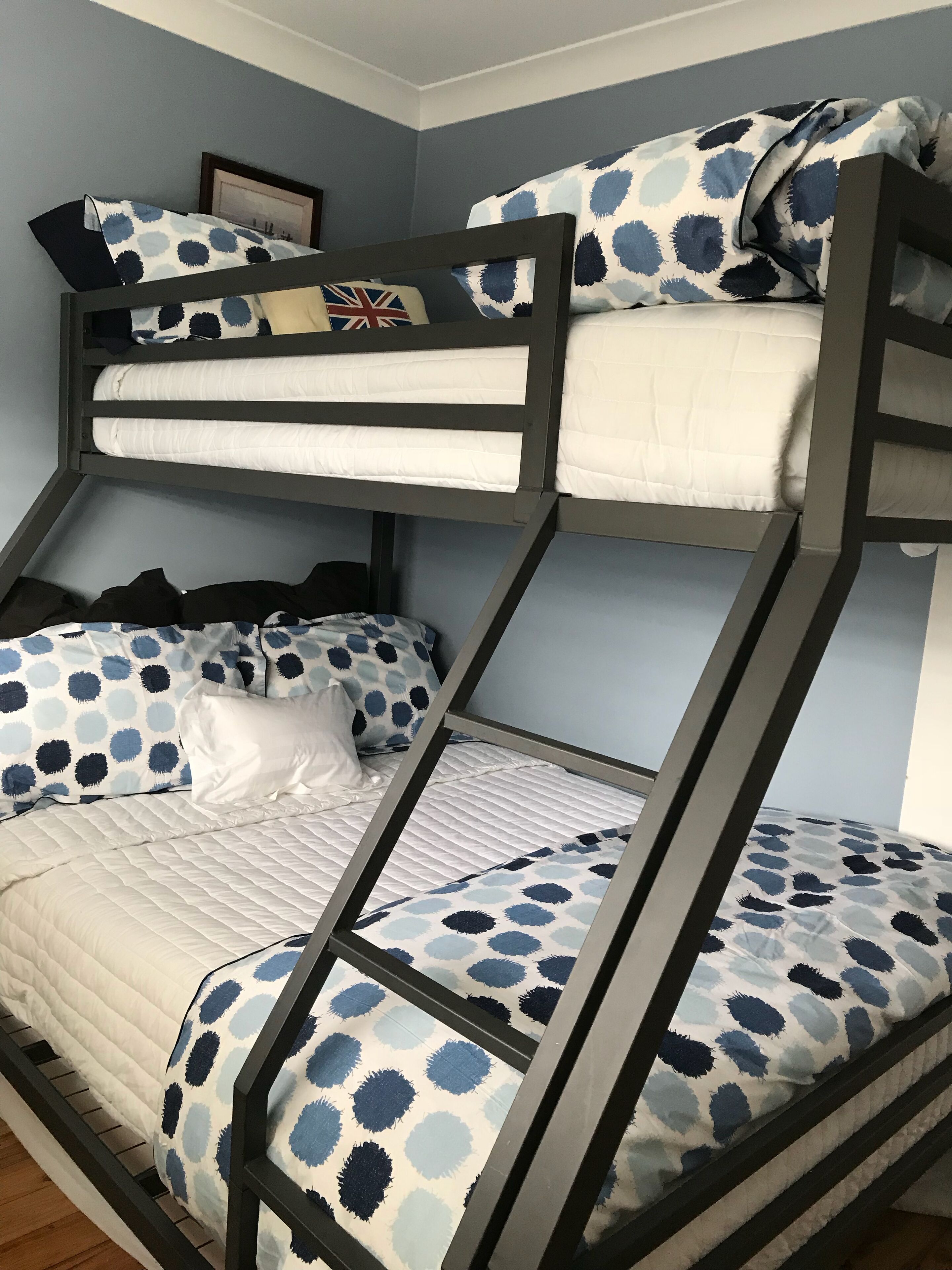 A bunk bed with a patterned bedspread and pillows, a framed picture on the wall, and a small shelf with books.
