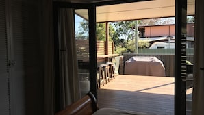 Habitación con puerta corrediza de vidrio que da a un patio exterior con una parrilla, cubierta de madera y zona de estar techada.