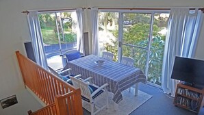 A dining area with a table and chairs, a television, and a staircase. - Jacaranda House where beach meets rainforest (Stanwell Park)