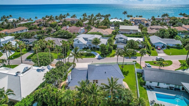 An aerial view of a coastal residential area with houses, palm trees, and a swimming pool.
