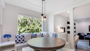 A modern living room with a round table, white sofas, and a large window with a view of greenery.