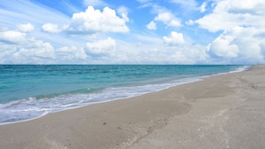 A beach with a sandy shore and calm sea under a partly cloudy sky.