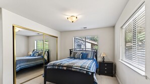 Een slaapkamer met een bed, een dressoir, een spiegel en een raam met jaloezieën.