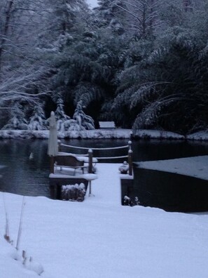 Un puente de madera cubierto de nieve sobre un cuerpo de agua, rodeado de árboles densos.