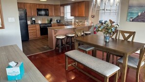 A modern kitchen with wooden cabinets, a central island, bar stools, and a dining table with benches. - BEACHFRONT LARGE SOUTHEND 3 BEDROOM 2 BATH CONDO (Brigantine)