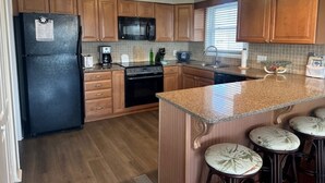 A kitchen with wooden cabinets, a black refrigerator, a microwave, a stove, and a granite countertop. - BEACHFRONT LARGE SOUTHEND 3 BEDROOM 2 BATH CONDO (Brigantine)