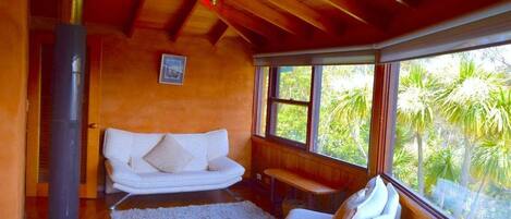 A cozy room with a white sofa, a bench, and a large window offering a view of greenery.