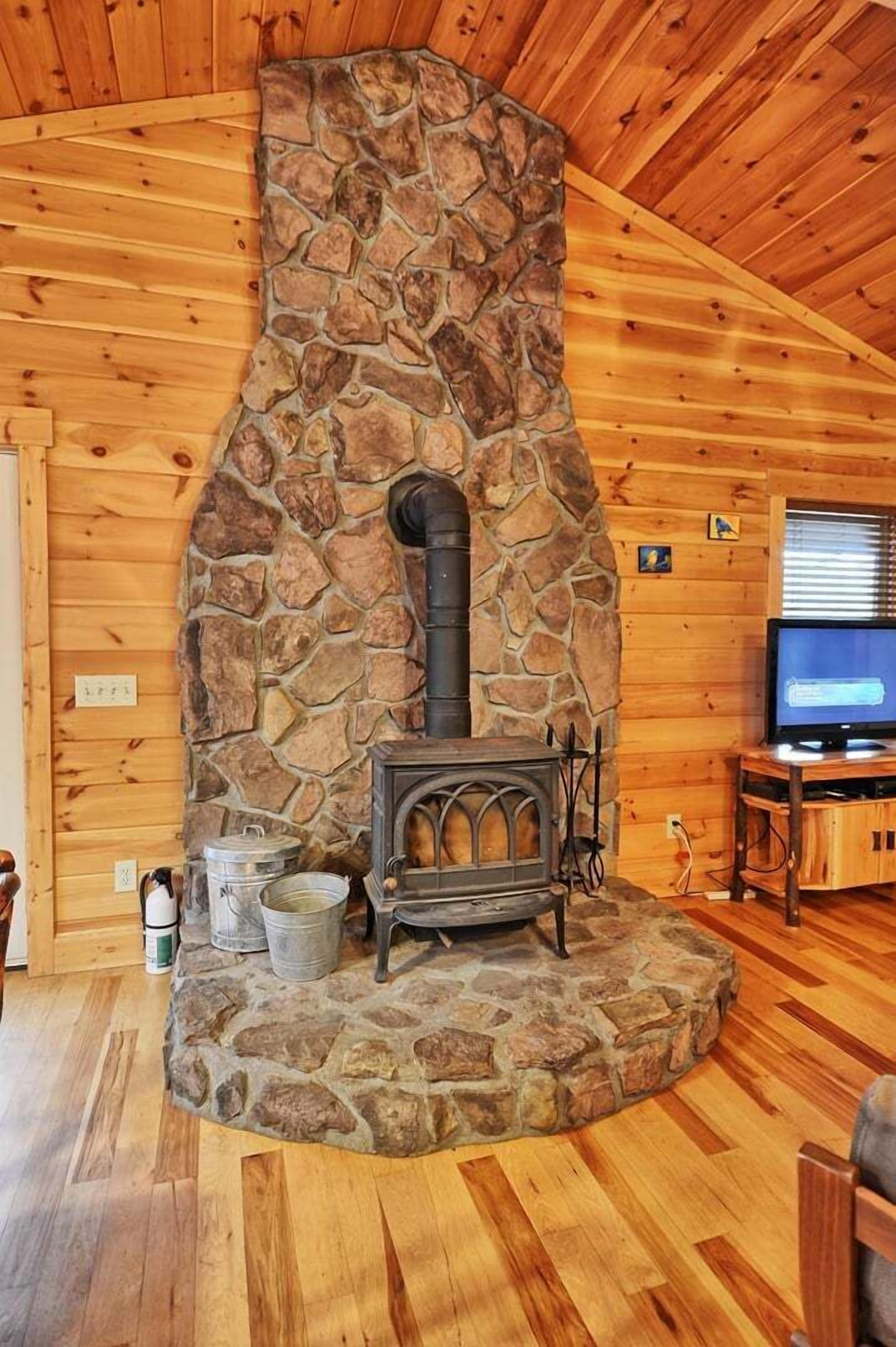A stone fireplace with a chimney, wooden walls, and a television on a wooden stand.