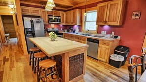 A kitchen with wooden cabinets, a central island with stools, a refrigerator, a microwave, a dishwasher, and a sink. - Experience comfort at Incommunicado in Warrensville, NC—a cozy 4-bedroom cabin for 10! (Warrensville)