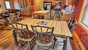 A rustic wooden interior with a dining table, chairs, a kitchen with appliances, and a living area with a couch. - Experience comfort at Incommunicado in Warrensville, NC—a cozy 4-bedroom cabin for 10! (Warrensville)