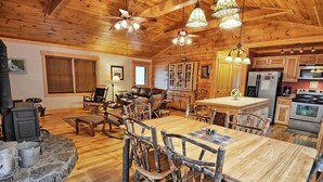 A rustic cabin interior with a wooden dining table, chairs, a fireplace, and a kitchen area. - Experience comfort at Incommunicado in Warrensville, NC—a cozy 4-bedroom cabin for 10! (Warrensville)