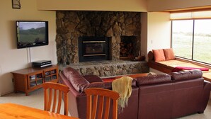 A living room with a stone fireplace, a television, a sofa, and a dining table with chairs. - OCEAN FRONT-WHITE WATER VU from every room - above Del Mar Cove (The Sea Ranch)