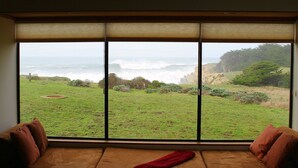 A room with a large window overlooking a grassy landscape and ocean. - OCEAN FRONT-WHITE WATER VU from every room - above Del Mar Cove (The Sea Ranch)