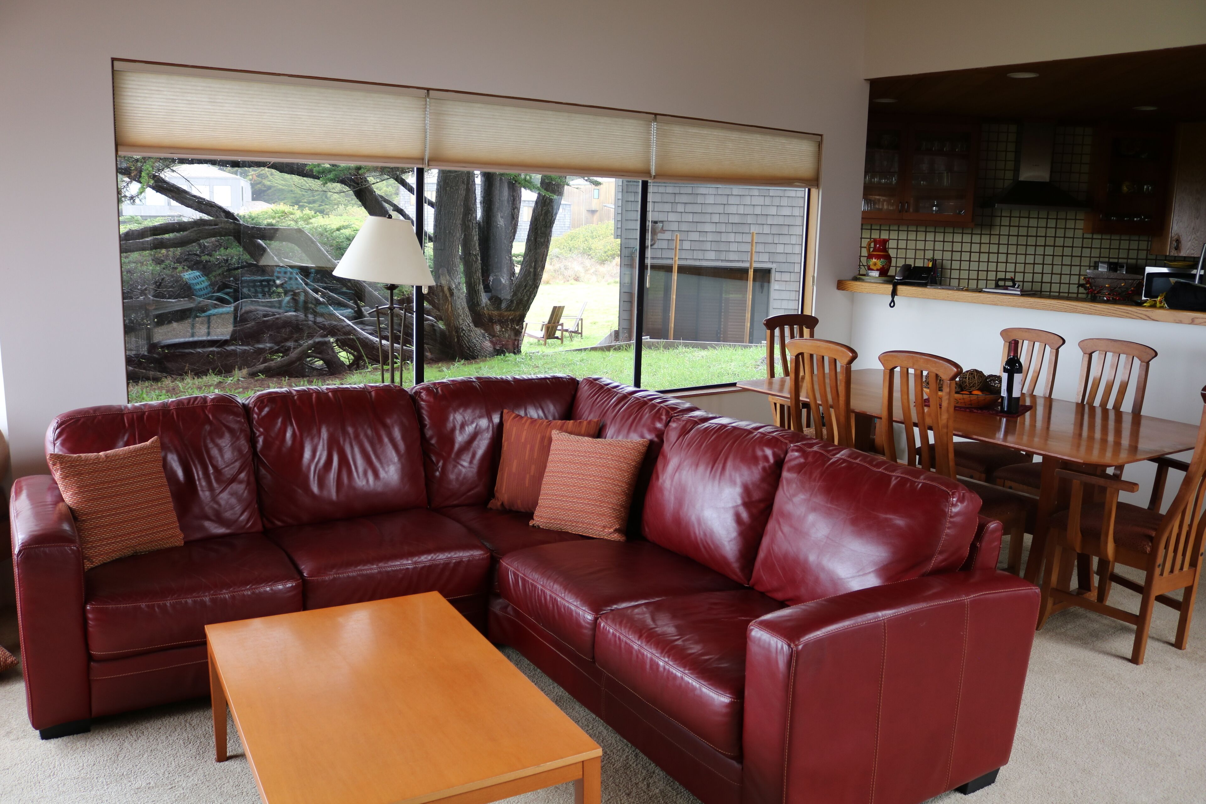 A living room with a red leather sectional sofa, a wooden coffee table, and a dining area with wooden chairs and a table.