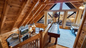 A wooden cabin with a loft bedroom, a dining area, and a view of the surrounding landscape.