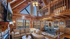 A spacious log cabin interior with a large living area, a dining table, and a cozy fireplace.