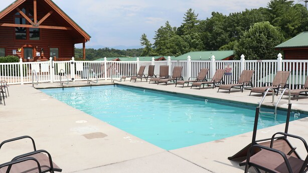 A pool area with lounge chairs and a wooden building in the background.