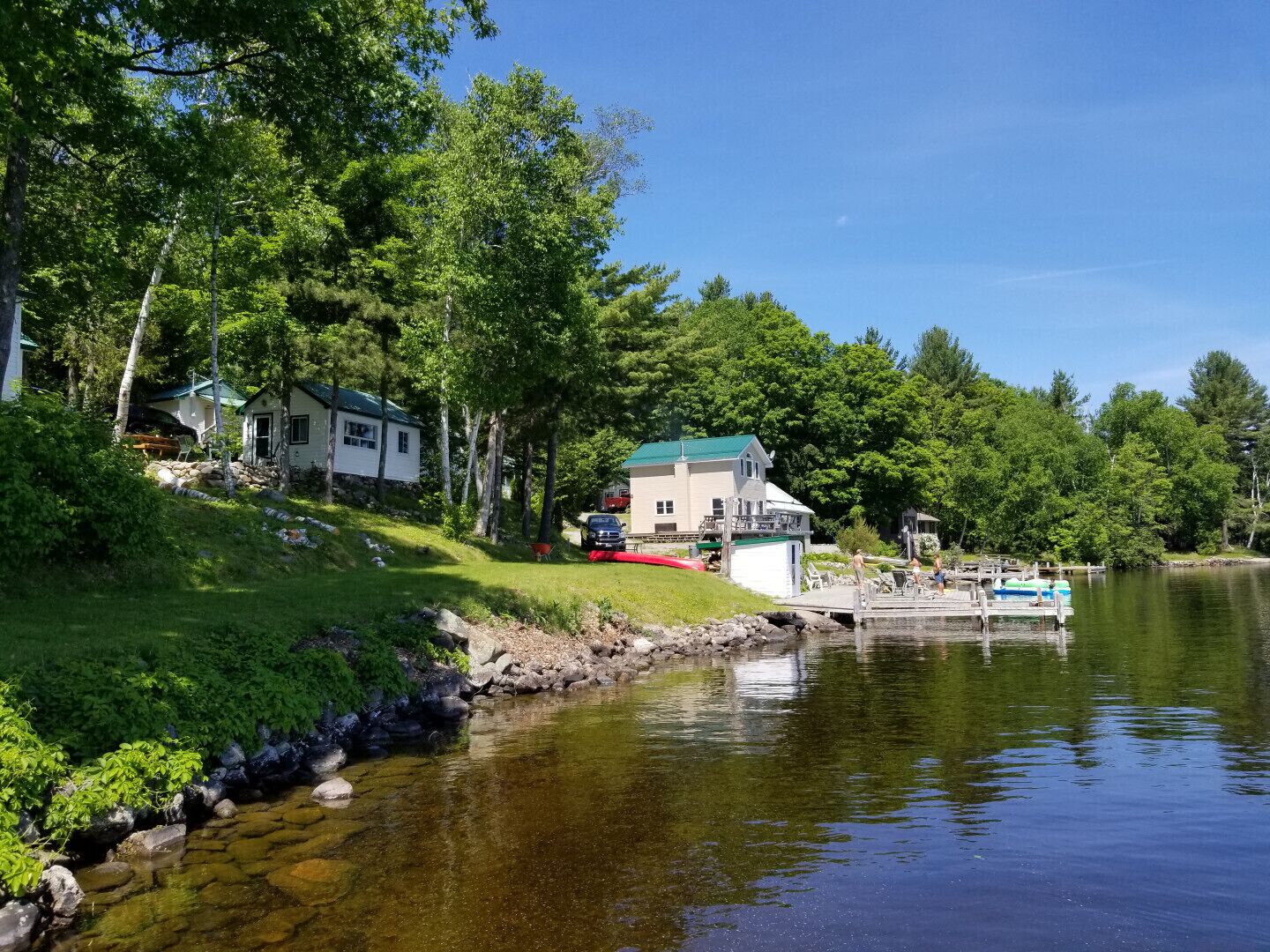 Une propriété au bord du lac, dotée d’un quai, d’une petite maison et d’un bâtiment plus grand avec un toit végétalisé.