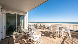 Un balcon avec vue sur la plage, des meubles d’extérieur et une porte vitrée donnant sur un espace intérieur.