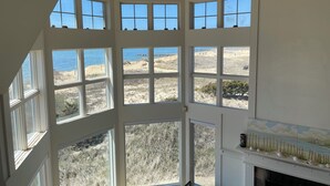 Habitació amb grans finestres múltiples que donen vista a l'oceà, una llar de foc i un sostre alt.