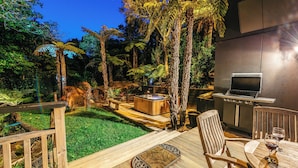 Eine Terrasse mit Holztisch und -stühlen, einem Whirlpool und einem Grill.