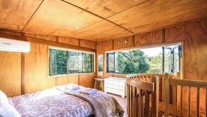 Ein Schlafzimmer mit Holzboden, einem Bett, einem Schminktisch und großen Fenstern mit Blick auf Grünflächen.