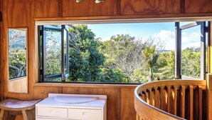 Ein Badezimmer aus Holz mit einem großen Fenster, einer Holzbank und einem weißen Waschbecken.