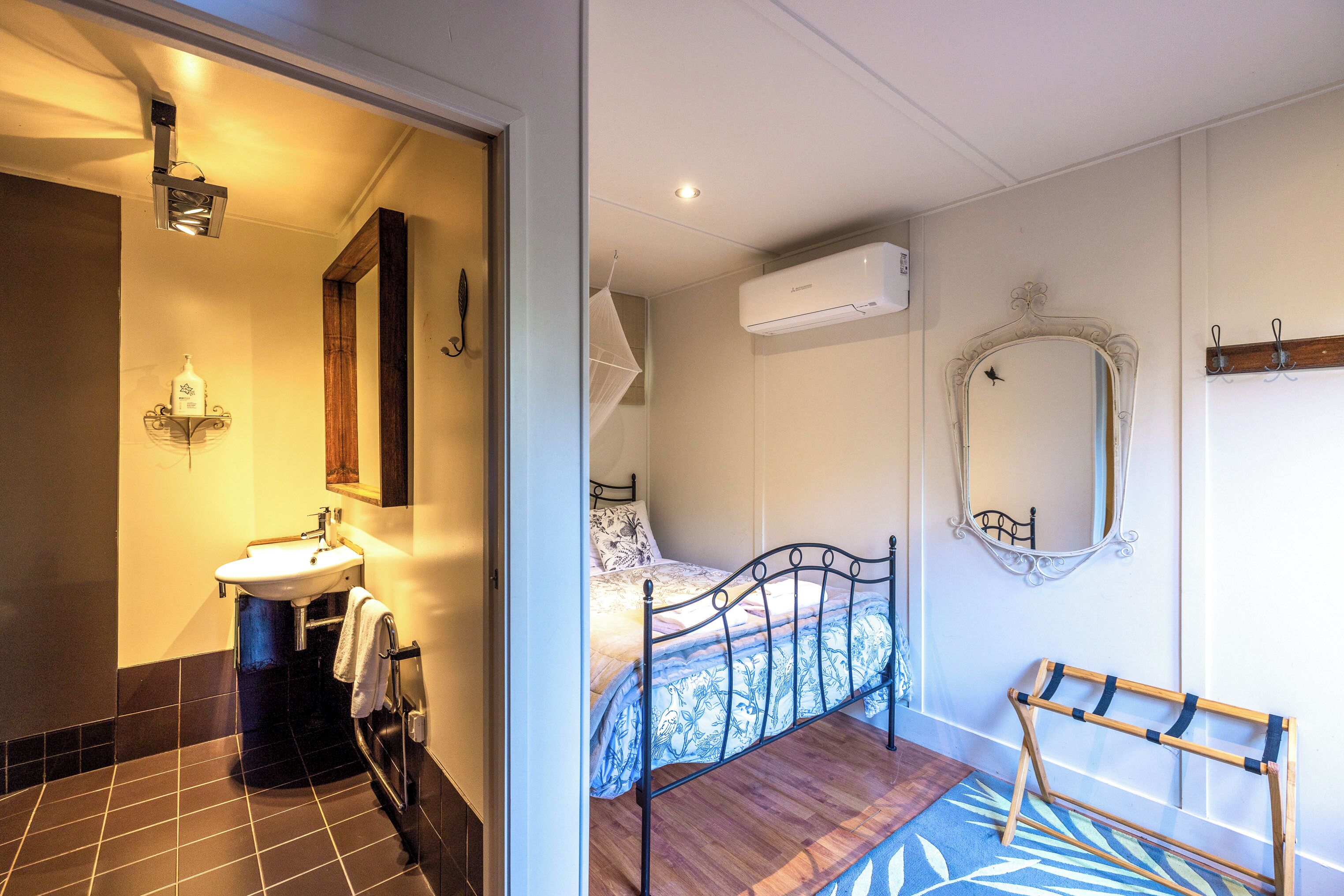 Une chambre à coucher comprenant un lit, une table de chevet, un miroir, un appareil de climatisation et une fenêtre.
