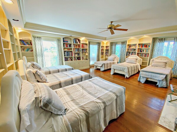 Quarto com quatro camas, ventilador de teto e estantes cheias de livros.