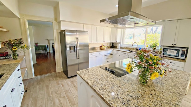 A modern kitchen with white cabinets, a stainless steel refrigerator, granite countertops, and a large island with a built-in stove. - Stunning House with Private Pool and Hot Tub on Rural Estate (Castleton)
