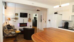 Una sala moderna con chimenea, un comedor con mesa de madera y una cocina con armarios blancos.