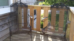 Una terraza de madera con dos sillas metálicas y una mesa de madera.