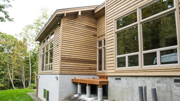 Ein modernes Gebäude mit horizontaler Holzverkleidung, großen Fenstern und einem Betonfundament.