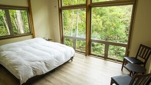 Ein Schlafzimmer mit einem Bett, einem Sessel und großen Fenstern mit Blick auf Grünflächen.