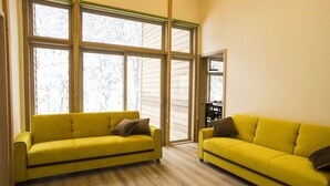 Ein Zimmer mit zwei gelben Sofas, großen Fenstern und Holzboden.