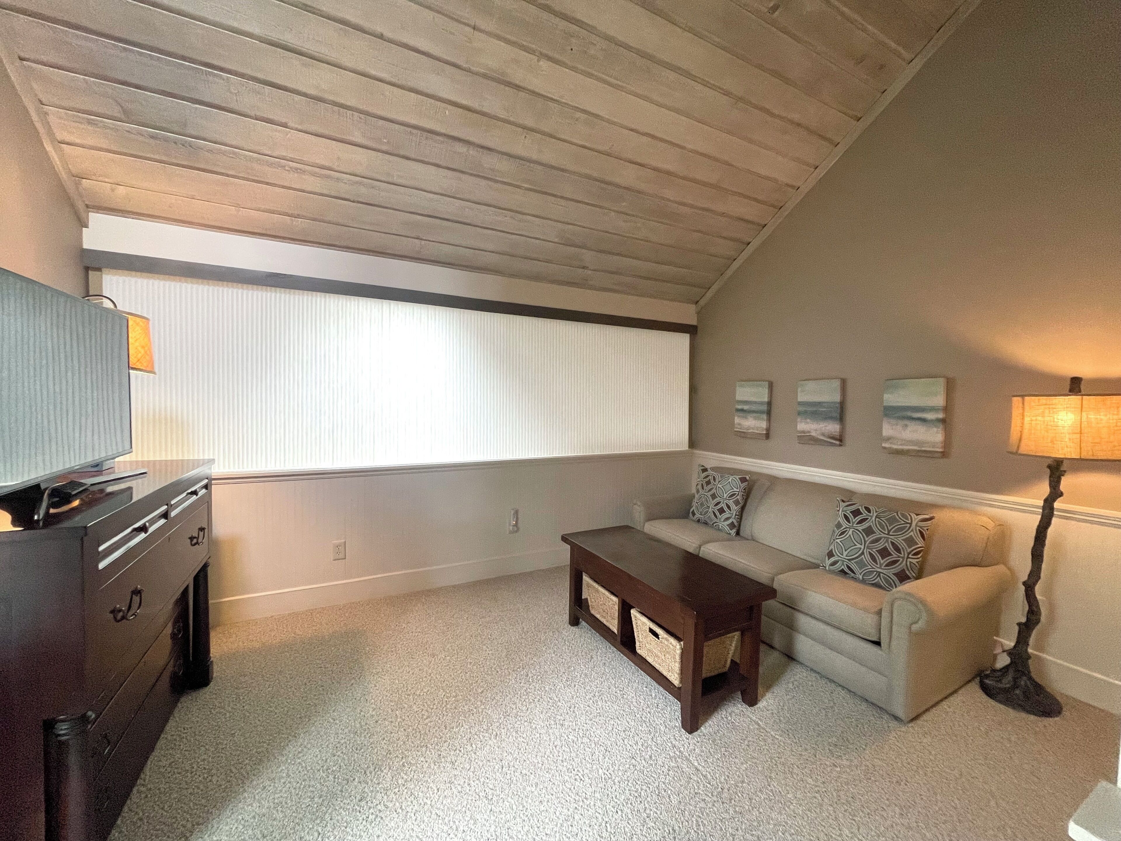 A living room with a sofa, a coffee table, a TV, and artwork on the wall.